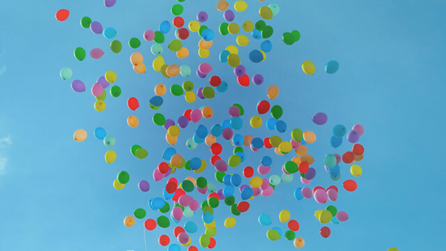 Mångfärgade ballonger som stiger mot en blå himmel