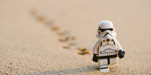 Fotografi på en legofigur i form av en Stormtrooper som går genom ett ökenlandskap med fotspår som försvinner bort i oskärpa bakom figuren i sanden.