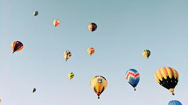 Fotografi upp mot en ljusblå himmel med ett flertal luftballonger som stiger mot nya höjder.