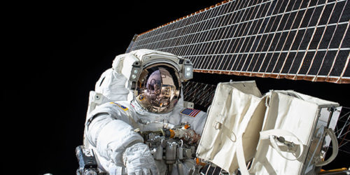 Fotografi från NASA på en astronaut som utför arbete vid ett par solpaneler ute i rymden.