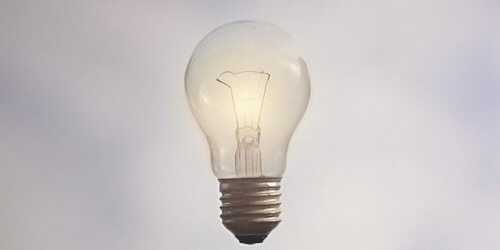 Fotografi på en tänd, svävande glödlampa mot en gråblå bakgrund.